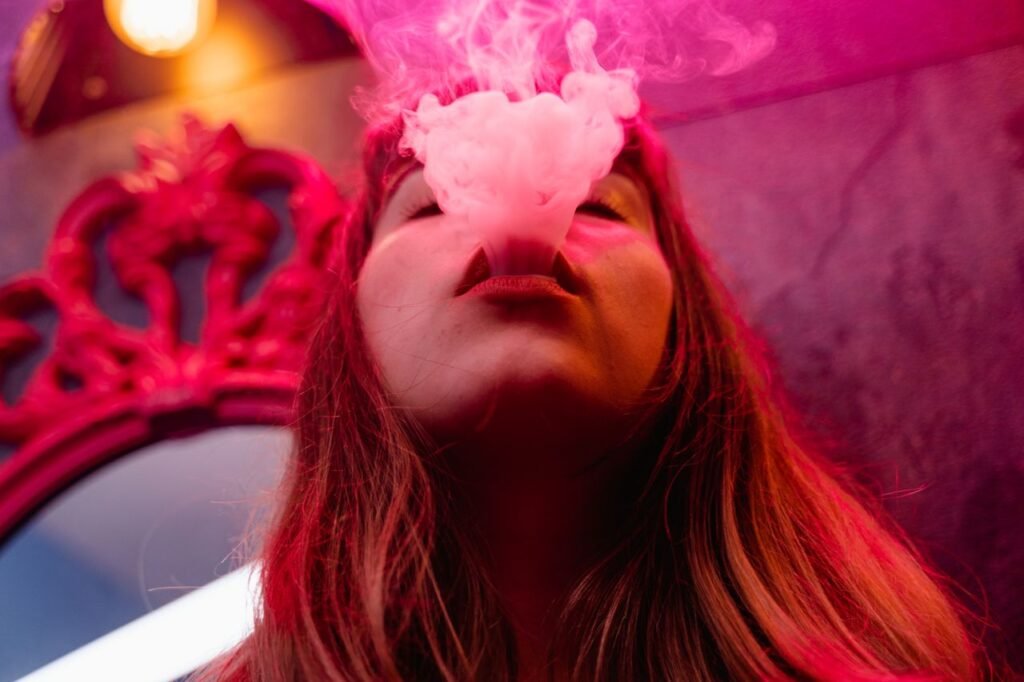 Close-up of a woman exhaling smoke with vibrant pink lighting creating a moody atmosphere.