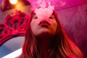 Close-up of a woman exhaling smoke with vibrant pink lighting creating a moody atmosphere.